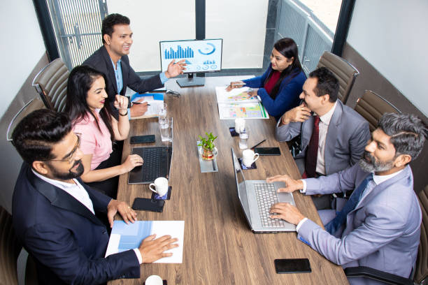 Indian business people meeting presentation in office conference room showing Charts Infographics on TV screen to show growth of company and big data analysis. E-Commerce e-Business. Top angle.